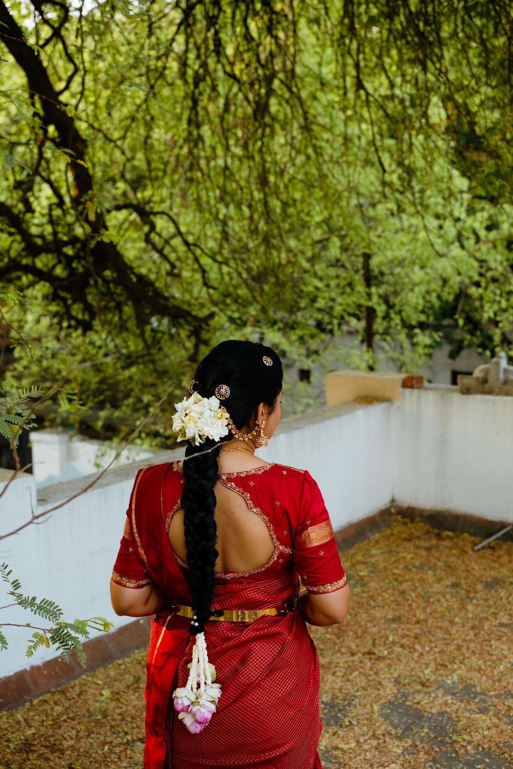 Back view of South Indian bride in red saree with intricate braid adorned with white flowers and gold hair accessories.