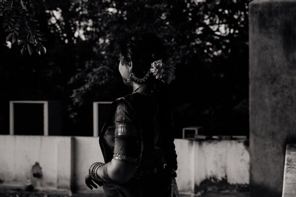 Black and white photo of a soldier in tactical gear standing outdoors near trees and a concrete wall.
