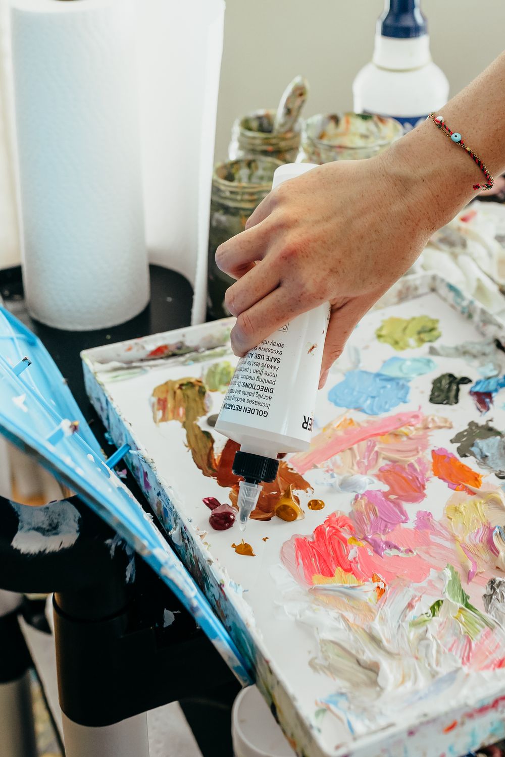 Artist squeezing colorful acrylic paint from a tube onto a well-used paint palette in an art studio.