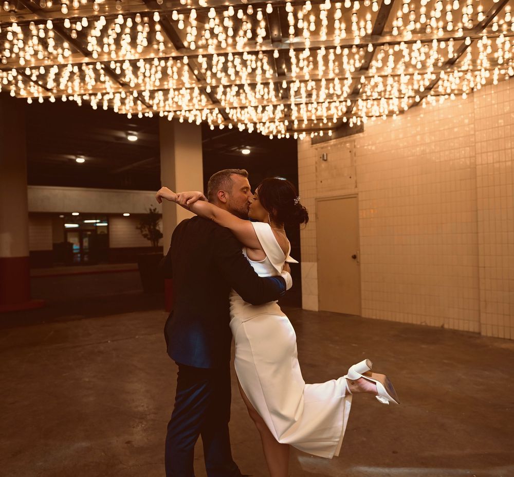 Couple sharing romantic kiss under warm string lights at wedding reception venue.
