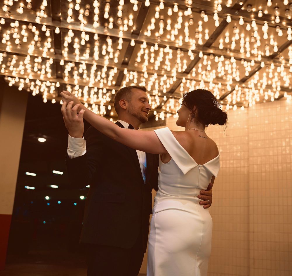 Bride and groom share first dance under sparkling chandelier lights at elegant wedding reception.