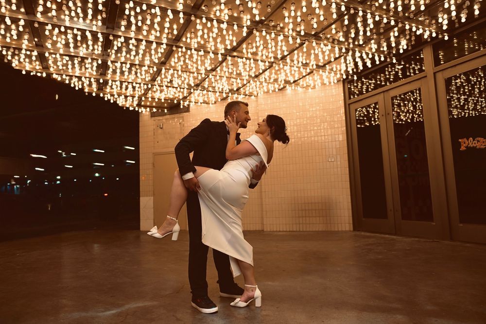 Couple sharing romantic dip dance under sparkling string lights at elegant wedding venue.