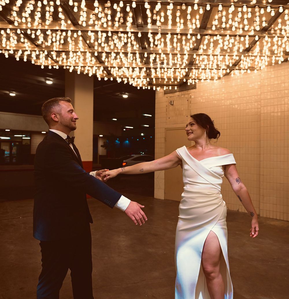 Couple in wedding attire dancing under sparkling chandelier lights in elegant venue.