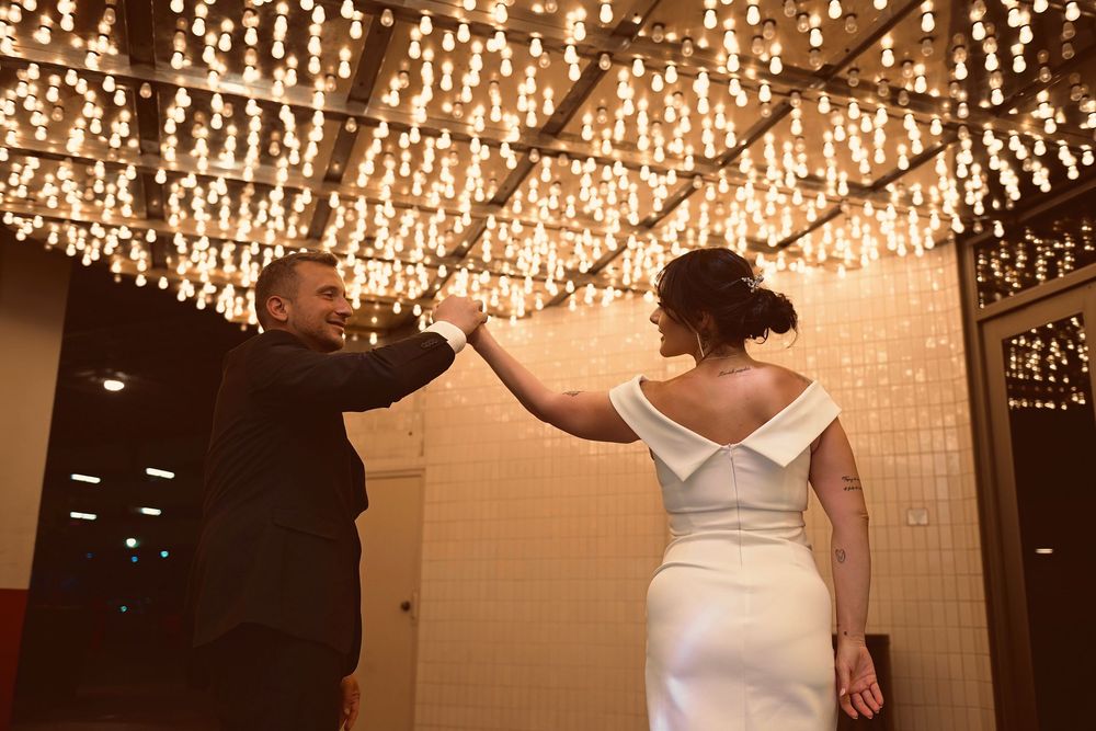 Bride and groom share first dance under glowing chandelier lights at elegant wedding reception venue.
