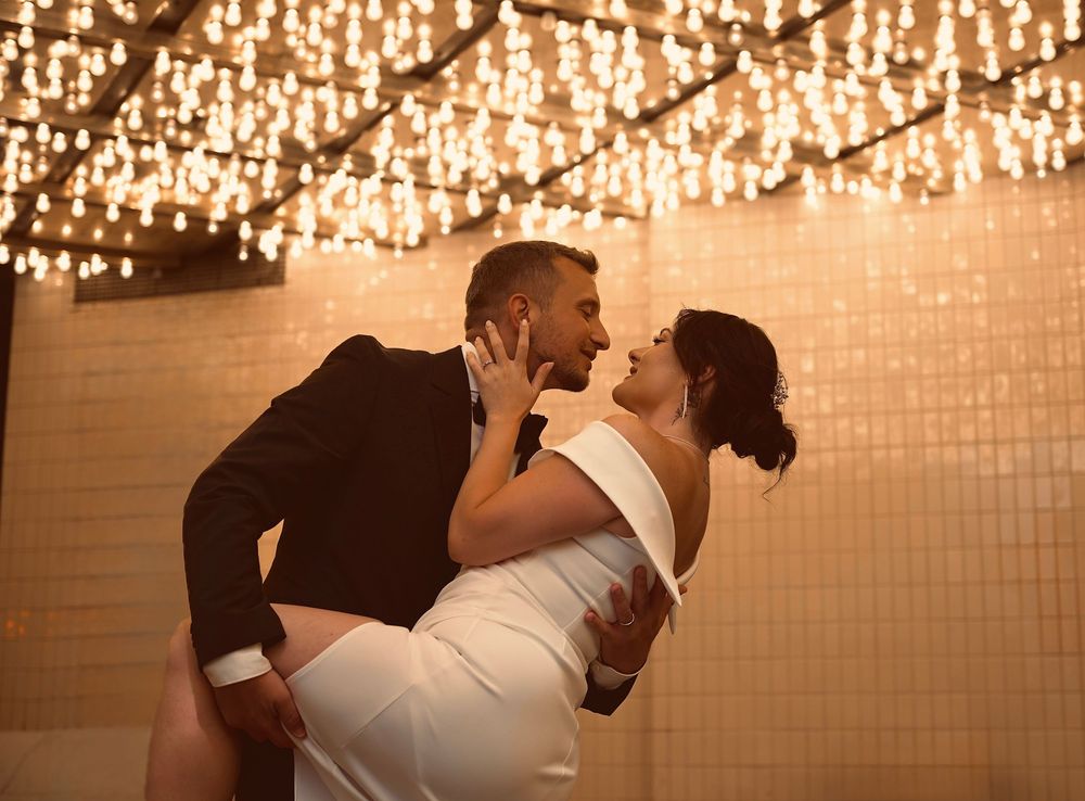 Bride and groom share a romantic dip kiss under warm glowing chandelier lights at elegant wedding venue.