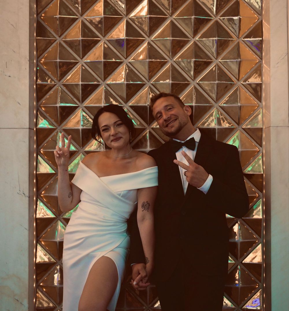 Bride and groom pose with peace signs in front of a gold geometric wall in Las Vegas.