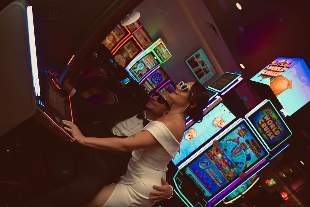Newlyweds kissing and taking selfie surrounded by colorful casino slot machines in Las Vegas.