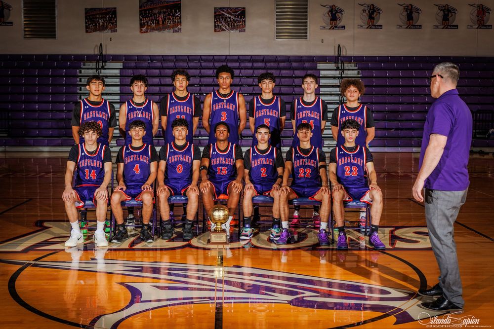 Youth basketball team in purple uniforms poses for official team photo on indoor court with trophy.