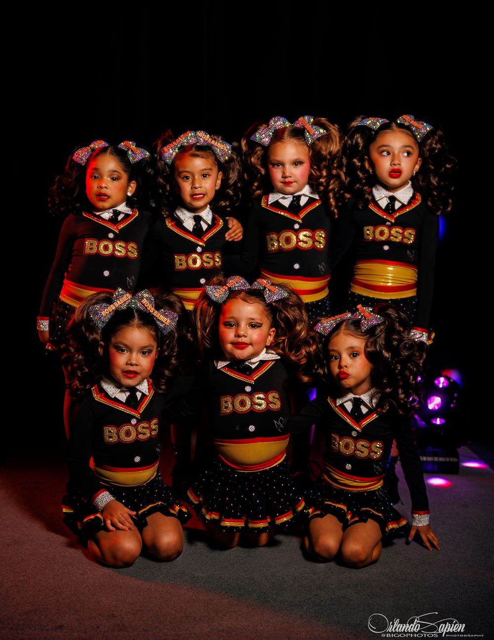 Seven young dancers in matching black and gold BOSS uniforms pose together on stage for a group portrait.