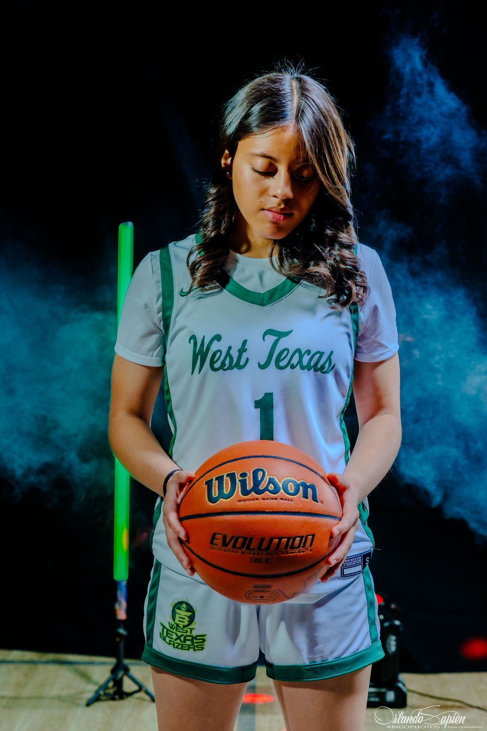 West Texas female basketball player #1 holding a Wilson Evolution basketball in a dramatic smoky arena setting.