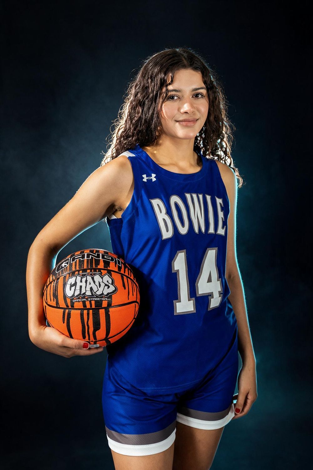 Smiling teen in Bowie #14 blue basketball jersey holds orange ball in studio.