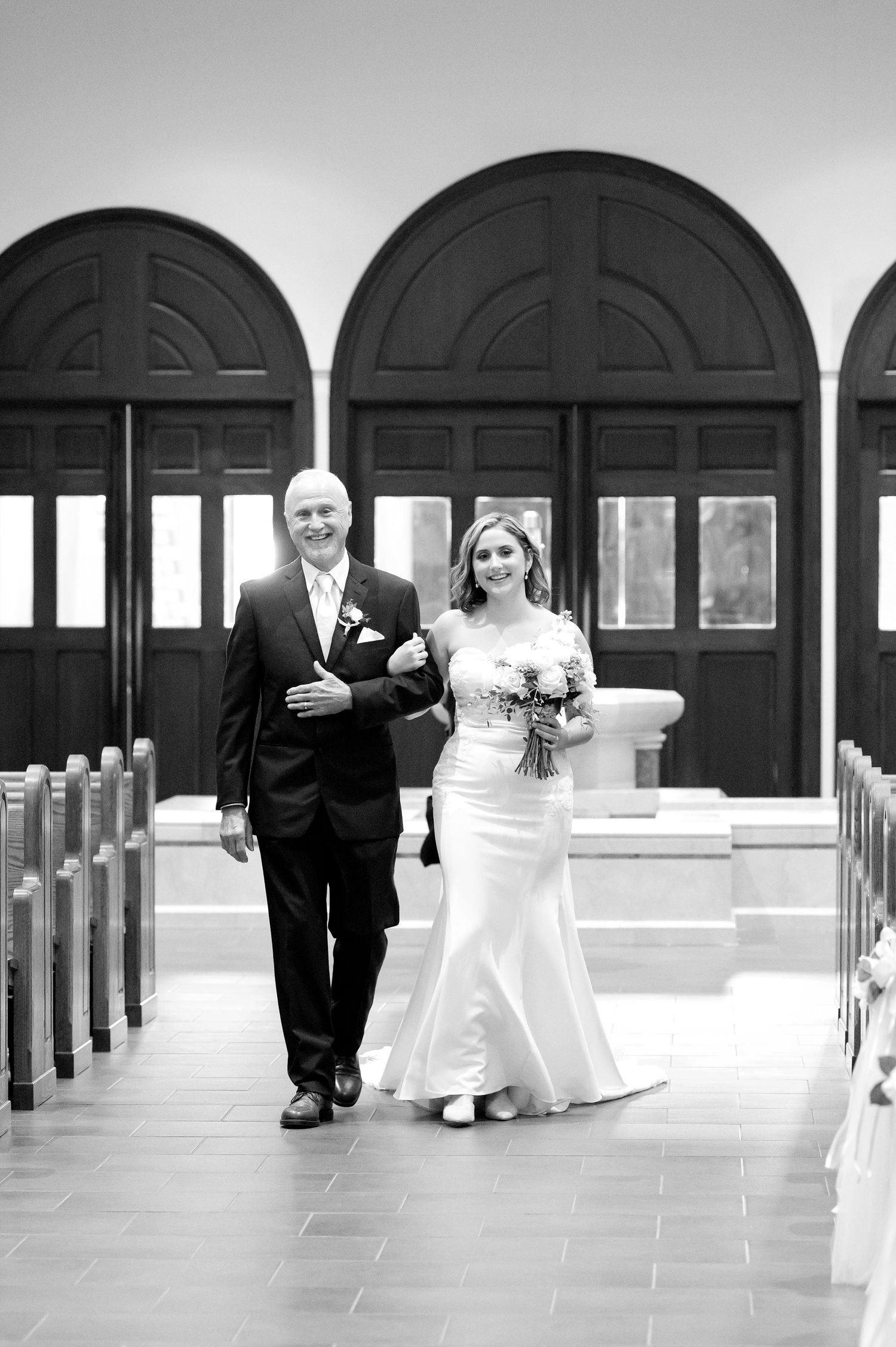 Black and white photo of a bride walking down the church aisle with her father on her wedding day.