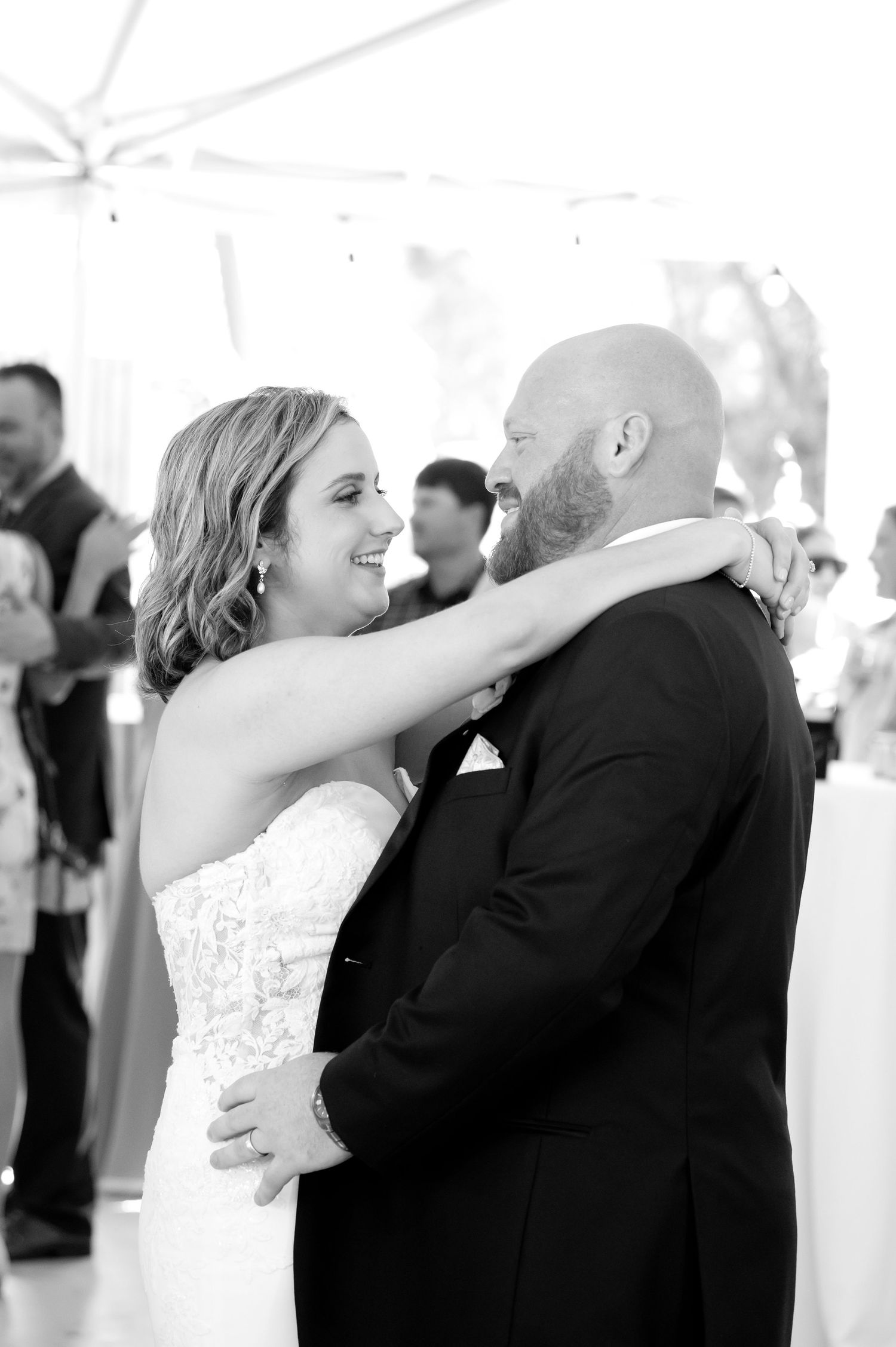 Black and white photo of bride and groom sharing first dance, smiling joyfully at wedding reception.