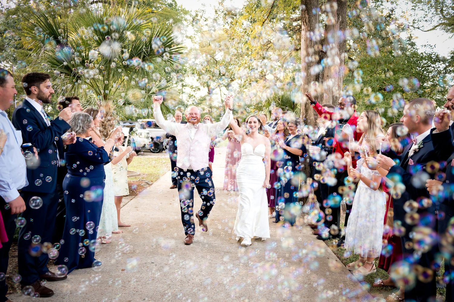 Joyful newlyweds walk through bubbles as guests celebrate their outdoor wedding ceremony.