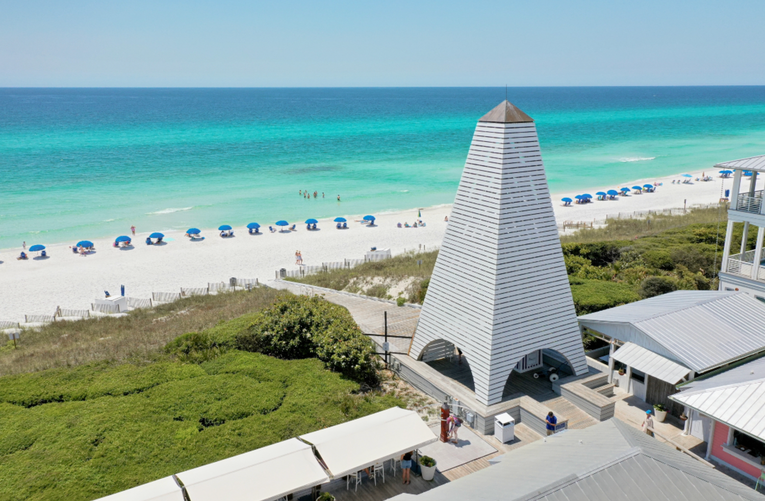 Aerial view of a white sandy beach with turquoise water, beach umbrellas, and a pyramid-shaped structure near Destin, Florida.