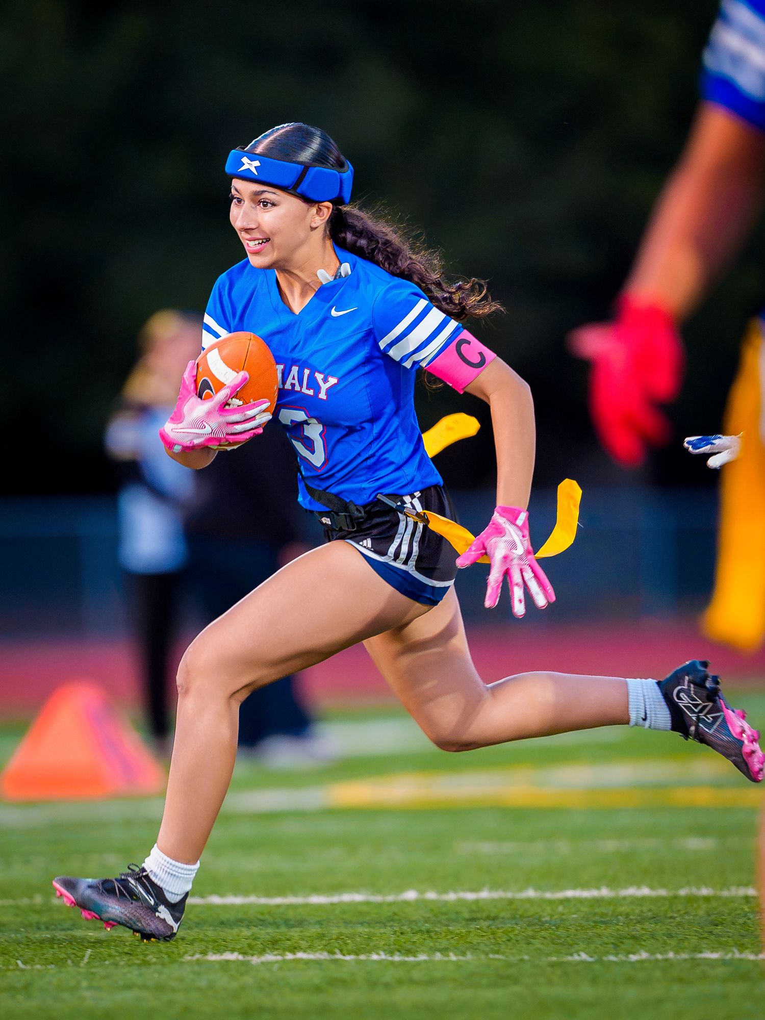 A female flag football player in a blue Italy uniform sprints with the ball during a game on a green field.