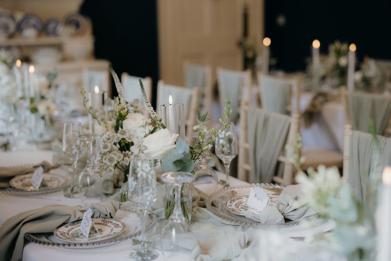 Elegant wedding reception table with white floral centerpieces, tapered candles, and soft gray linens.