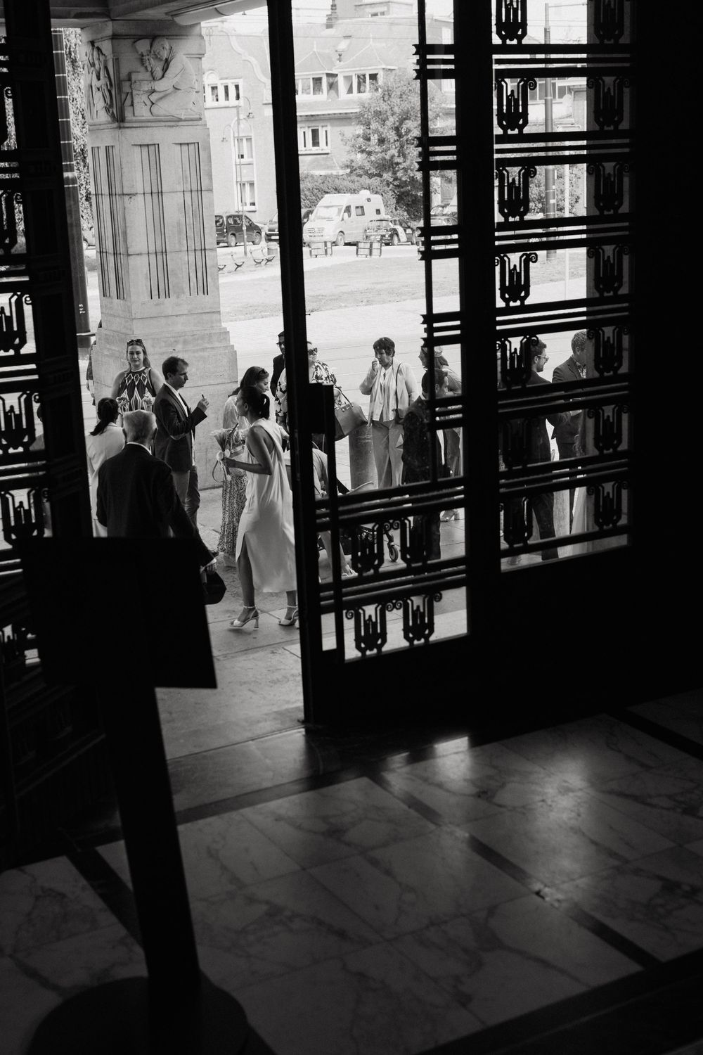 Black and white photo of wedding guests gathered at ornate doors of a grand building entrance.
