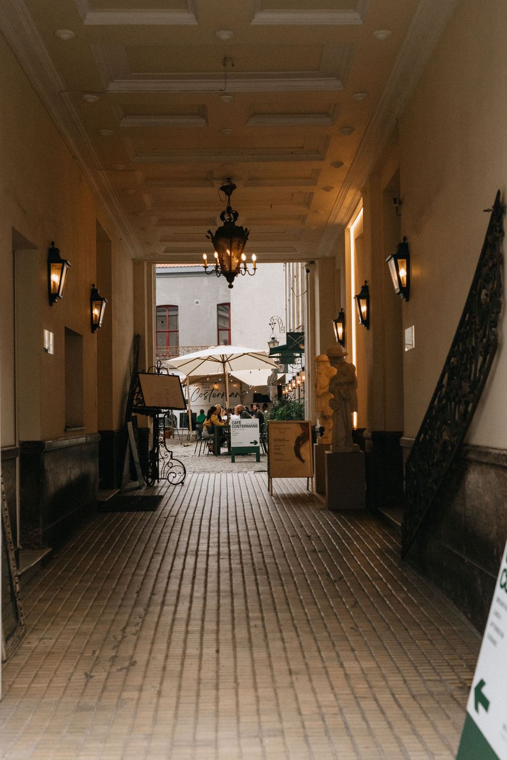 Elegant corridor with chandelier and wall sconces leading to an outdoor patio with white umbrella tables.