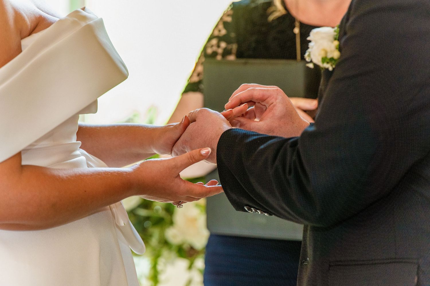 Groom placing a wedding ring on bride's finger during outdoor ceremony.