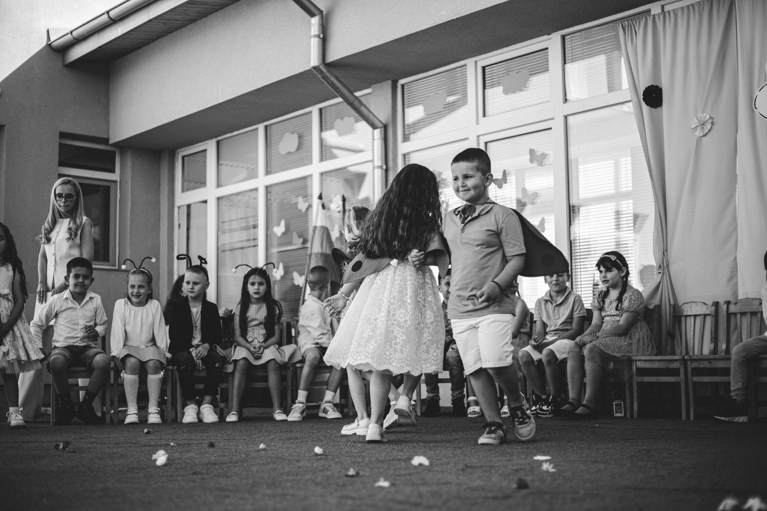 Black and white photo of children dancing at a school event while classmates watch seated along the wall.