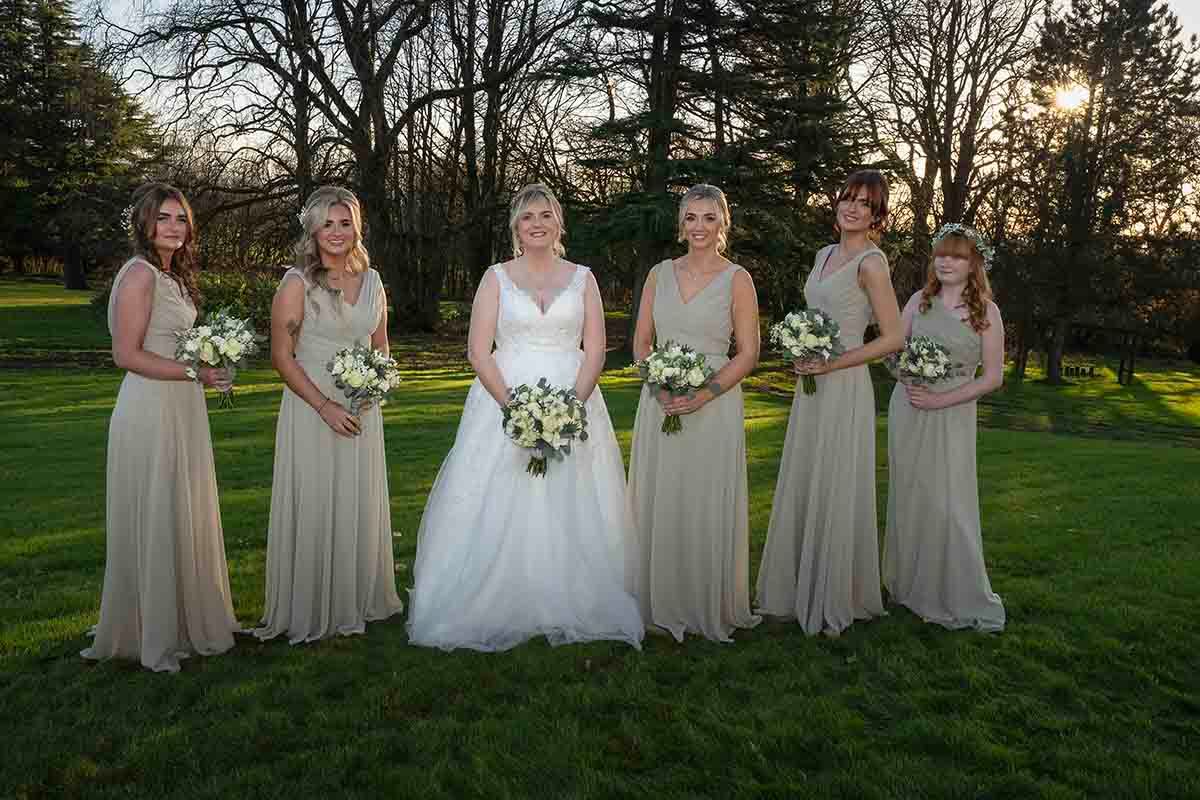 Bride in white gown poses with five bridesmaids in the wooded area at Hetland hall Dumfries & Galloway
