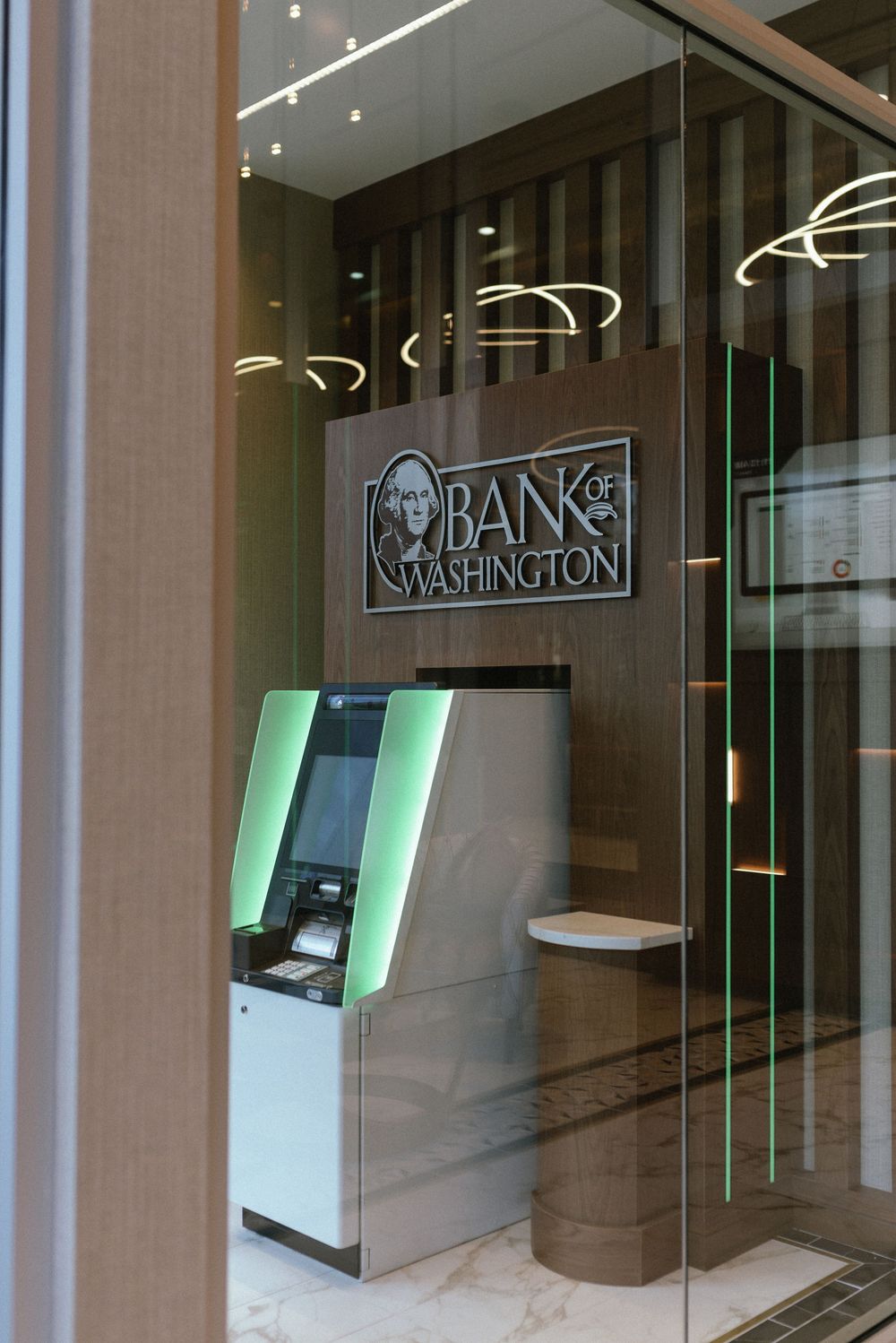 Bank of Washington branch interior featuring a modern ATM with green lighting and sleek wood-paneled walls.