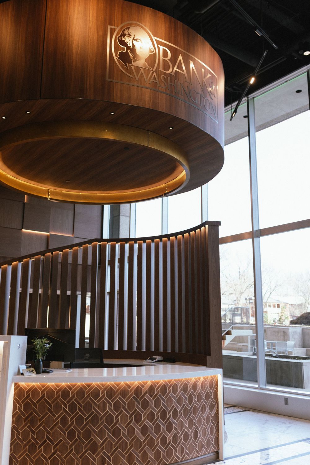 Modern bank lobby with curved wood staircase, illuminated reception desk, and large windows at Bank of Washington.