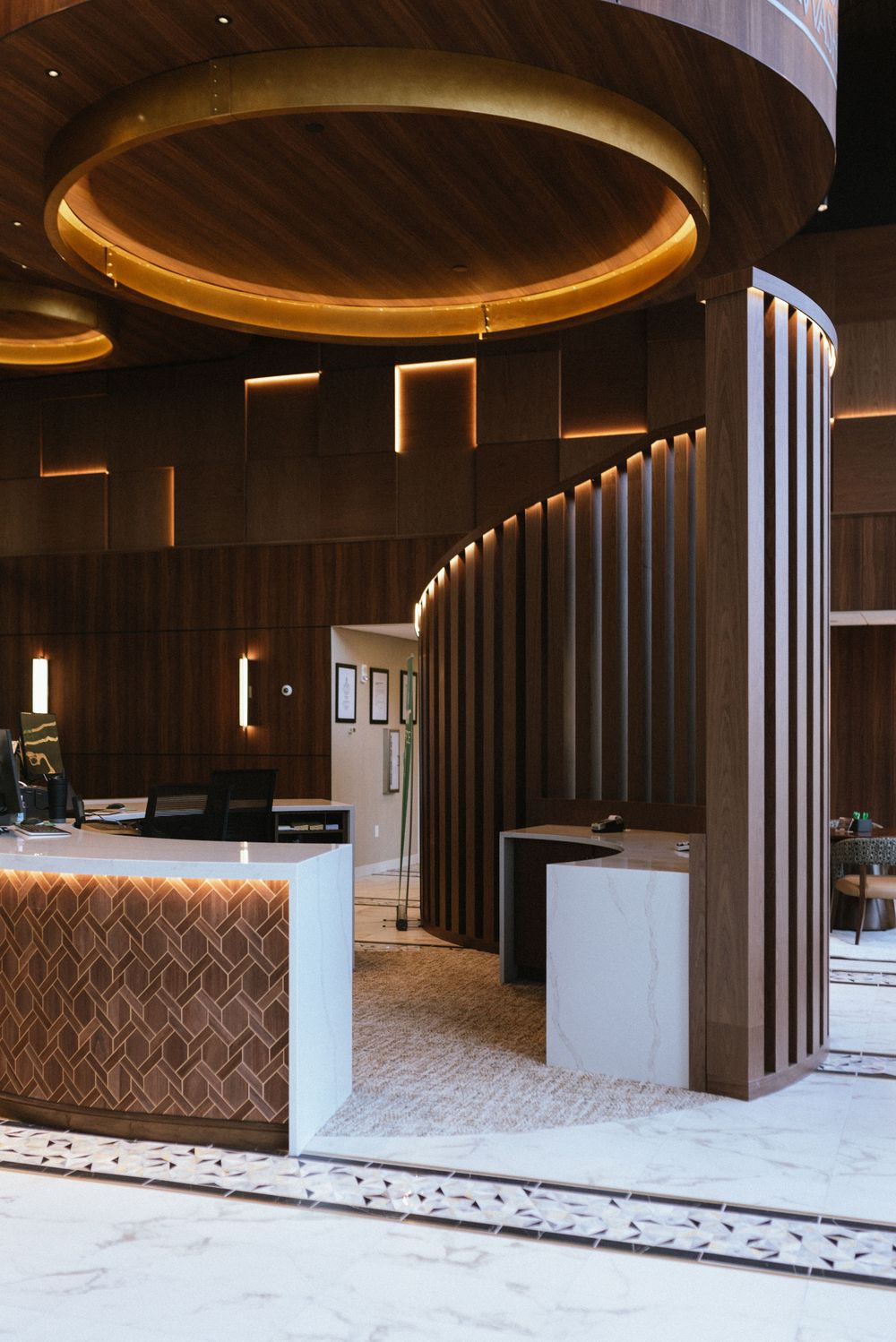 Luxurious hotel lobby with warm wood paneling, circular ceiling detail, marble floors, and elegant reception desk.