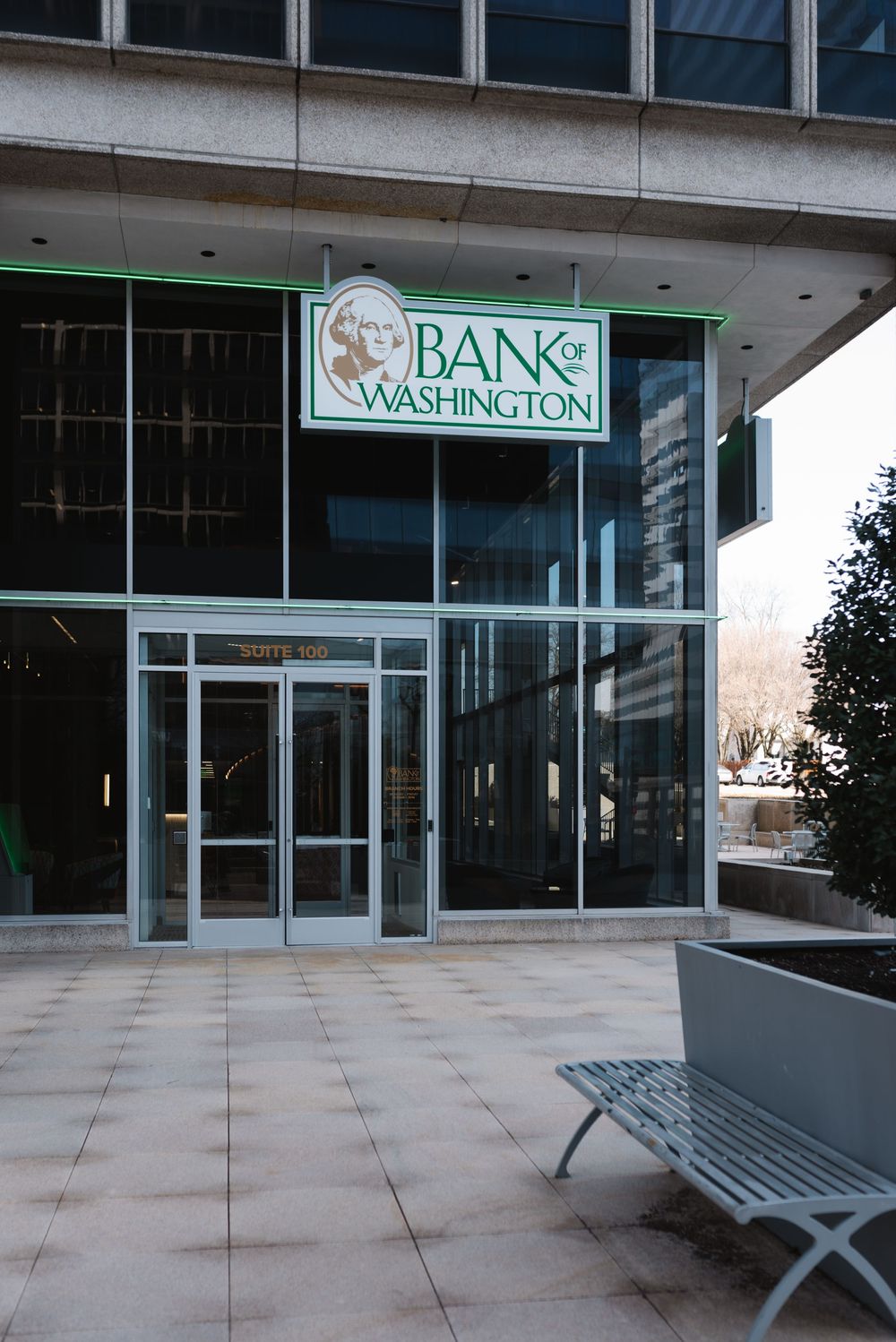 Bank of Washington branch entrance with glass doors, green signage, and a metal bench on a tiled plaza.