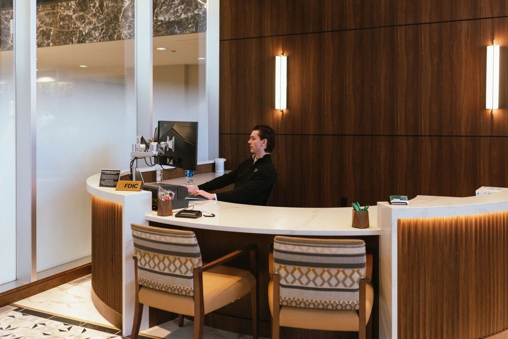 Elegant hotel reception desk with a suited concierge attendant seated at a curved wooden front desk.