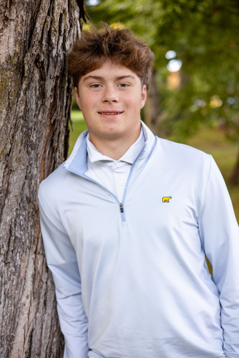 Boy smiling for senior photo next to a tree