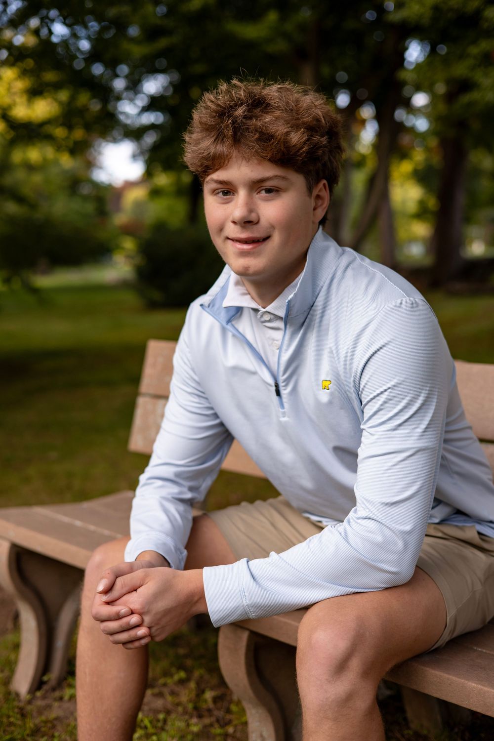 High school senior sitting on a bench smiling for outdoor portrait in Wilbraham, MA