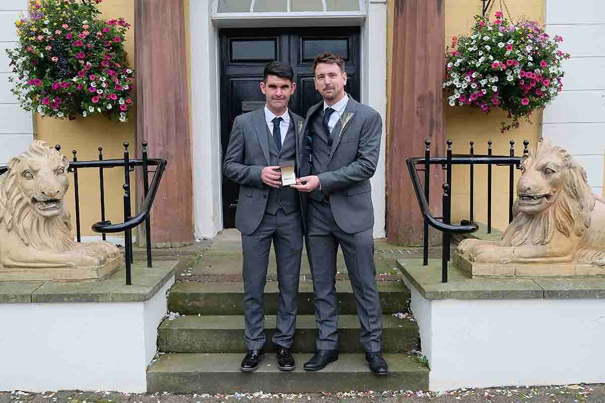 Groom & best man in grey suits posing together on steps outside Cockermouth town hall wedding venue