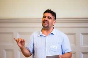 Man with name tag speaking and gesturing at a professional development workshop.
