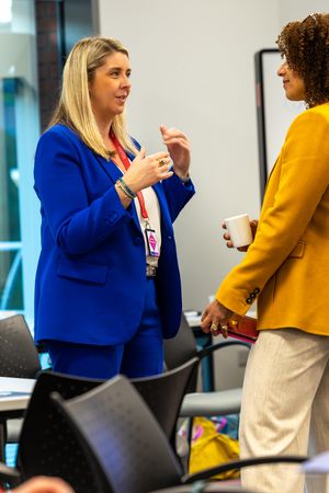 Woman in blue suit gestures while conversing with colleague in yellow blazer during professional networking event.