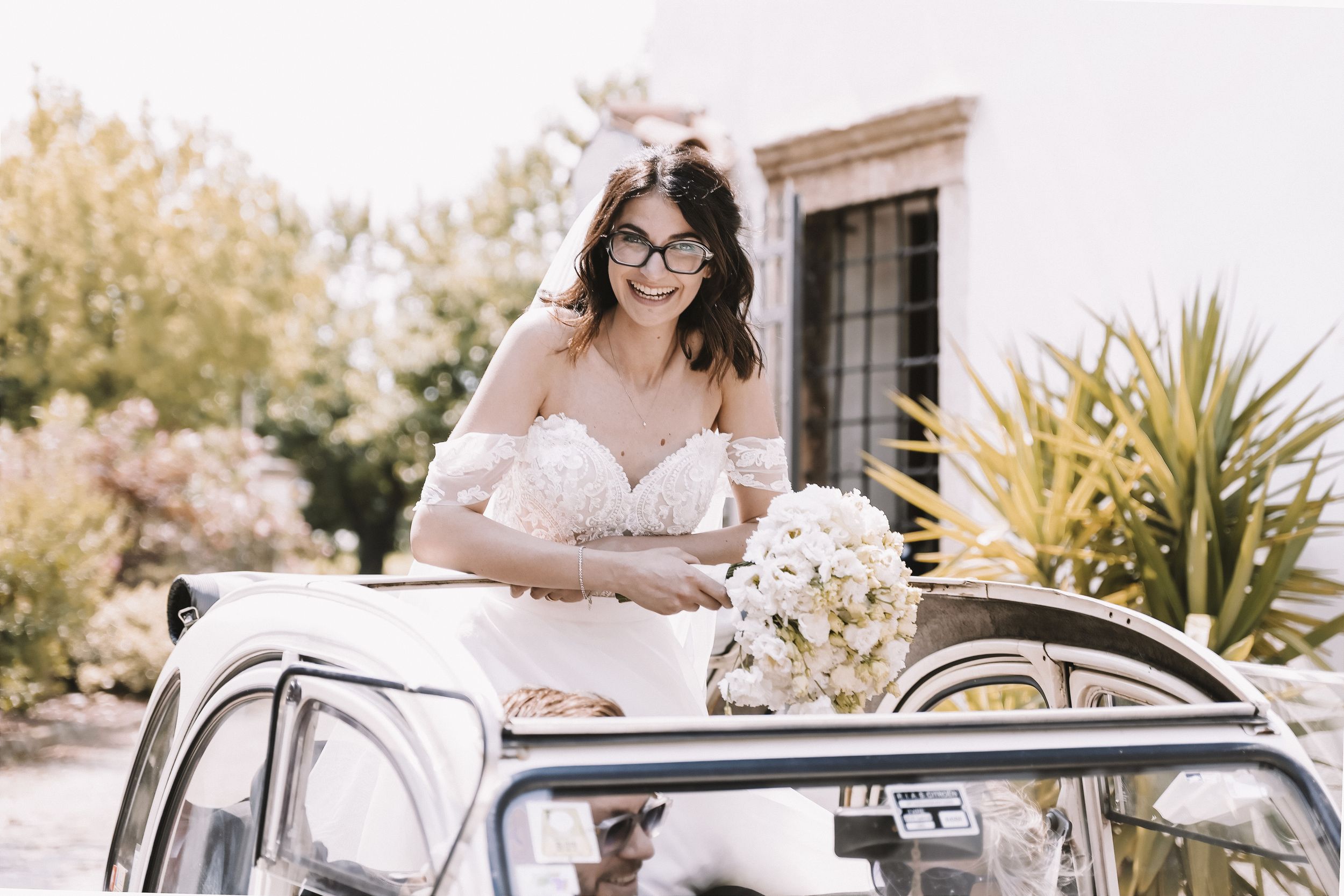 Sposa sorridente accanto all’auto con il bouquet