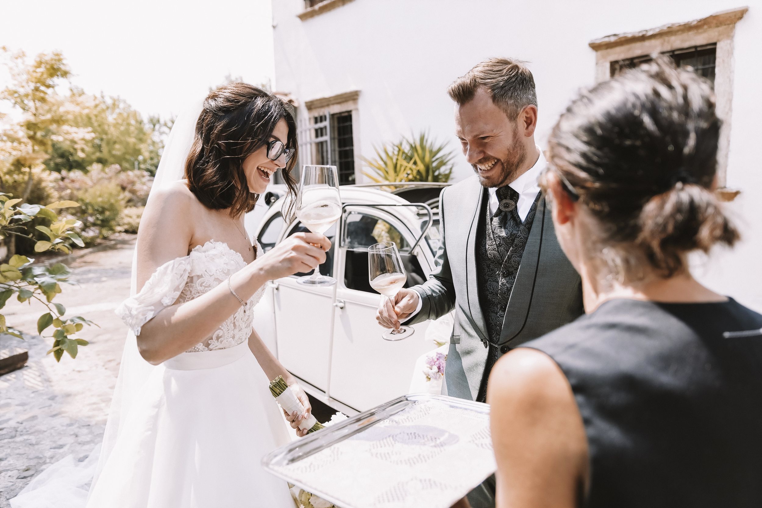 Sposa e sposo brindano accanto all’auto durante il matrimonio