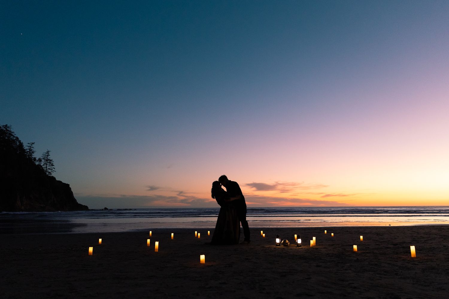 Romantic couple silhouetted against a sunset beach, surrounded by glowing candles arranged on the sand.