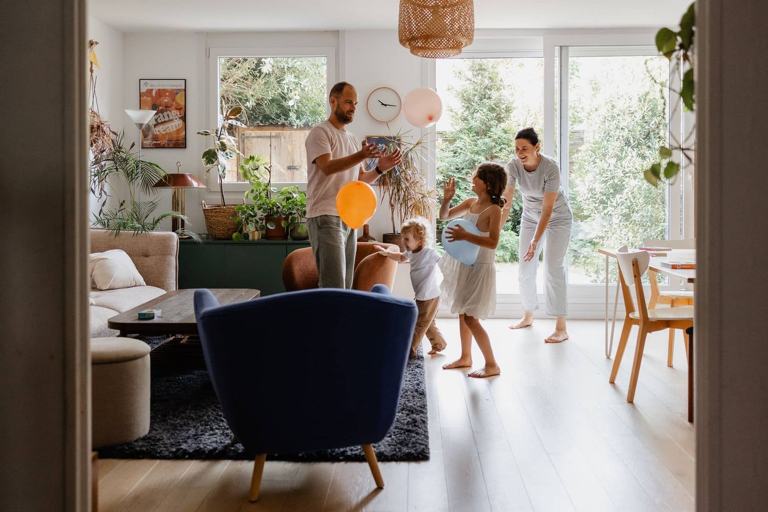 Photographe famille a domicile a Lille, parents et enfants riant ensemble en jouant aux ballons dans un salon baigne de lumiere naturelle