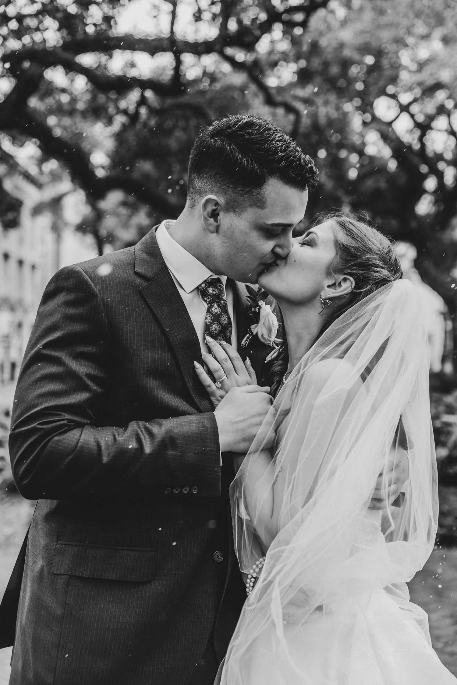 Black and white photo of a bride and groom sharing a romantic kiss outdoors on their wedding day.