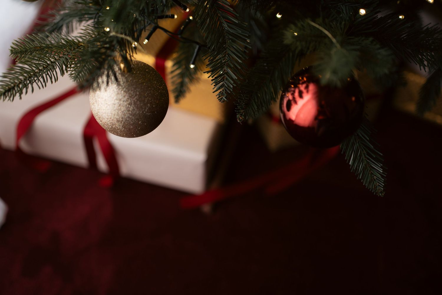 Festive Christmas living room with decorated tree, white fireplace filled with candles, wreath, and gifts against red walls.