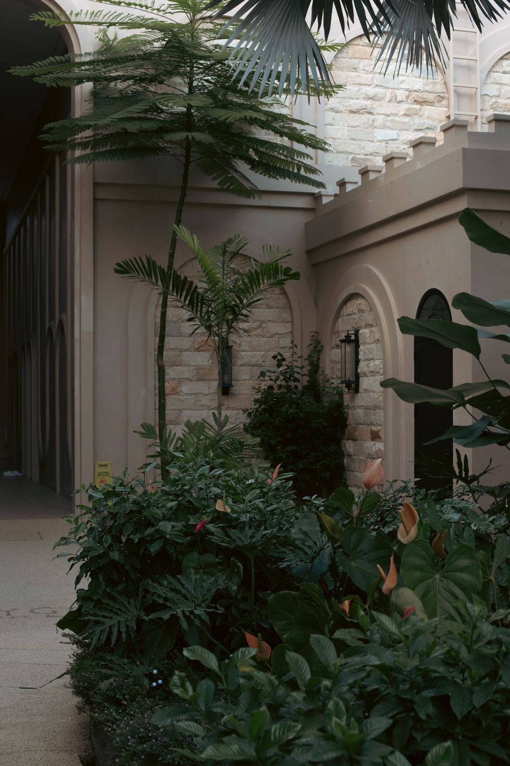 Lush tropical plants and palm trees surround an elegant stone archway in a serene courtyard garden.