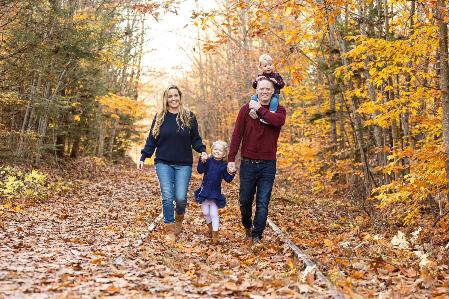 Happy family walking through colorful autumn forest trail covered in fallen leaves. Cotton Valley Rail Trail Wolfeboro NH