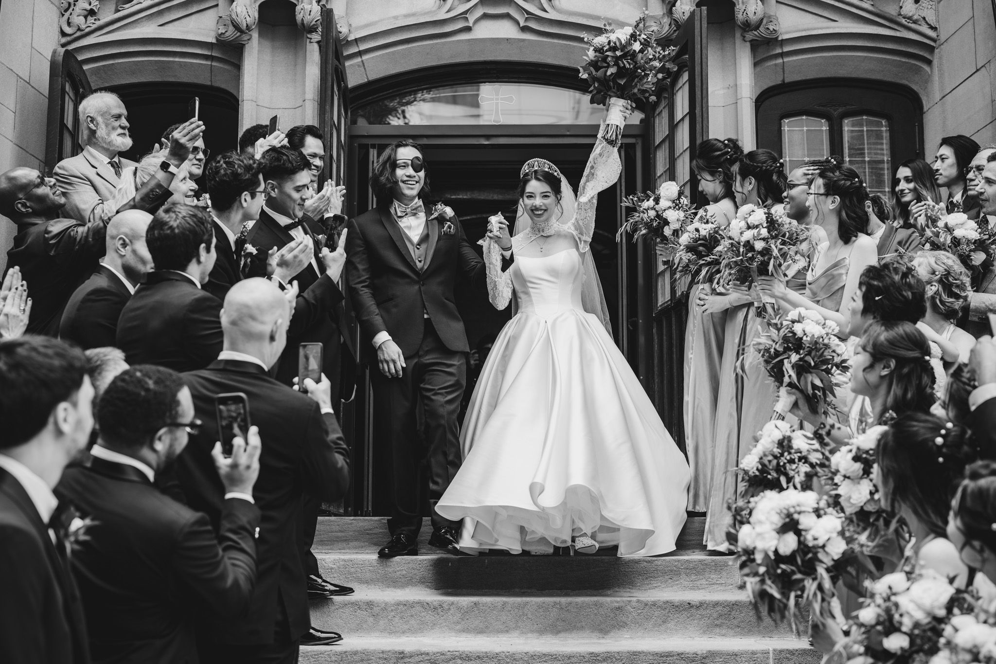Wedding guests celebrate and cheer as newlyweds exit the church after their ceremony.