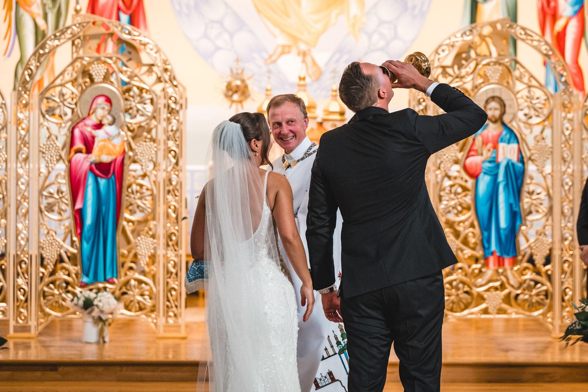 Romantic couple shares their first dance in an ornate gold ballroom with elegant decor and lighting.