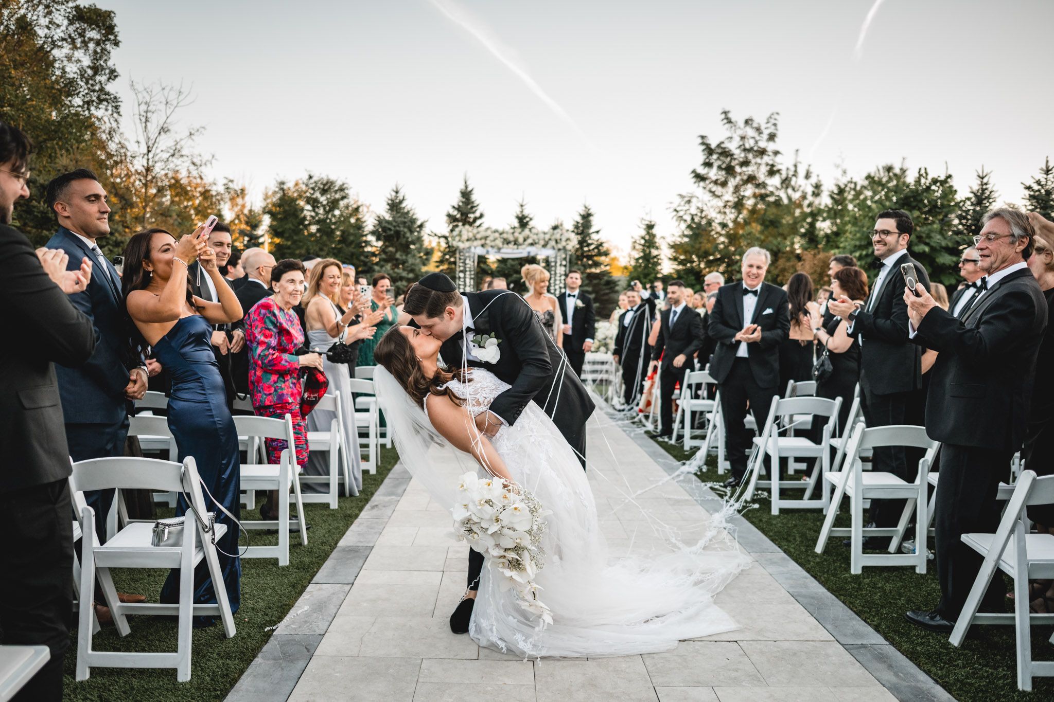 A wedding ceremony setup outdoors with white chairs arranged in rows and floral decorations at sunset.