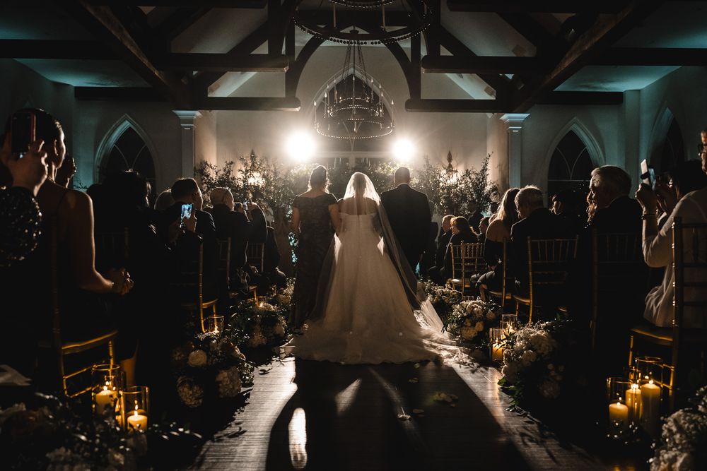 Silhouetted wedding couple walks down a dramatically lit church aisle with guests seated on both sides.