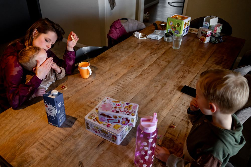 Children sitting at a wooden table with snacks, juice boxes, and a puzzle box in a home setting.