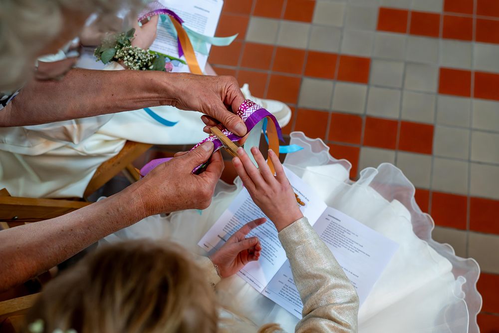 Hands tying colorful ribbons on a wedding dress during a bridal ceremony preparation.